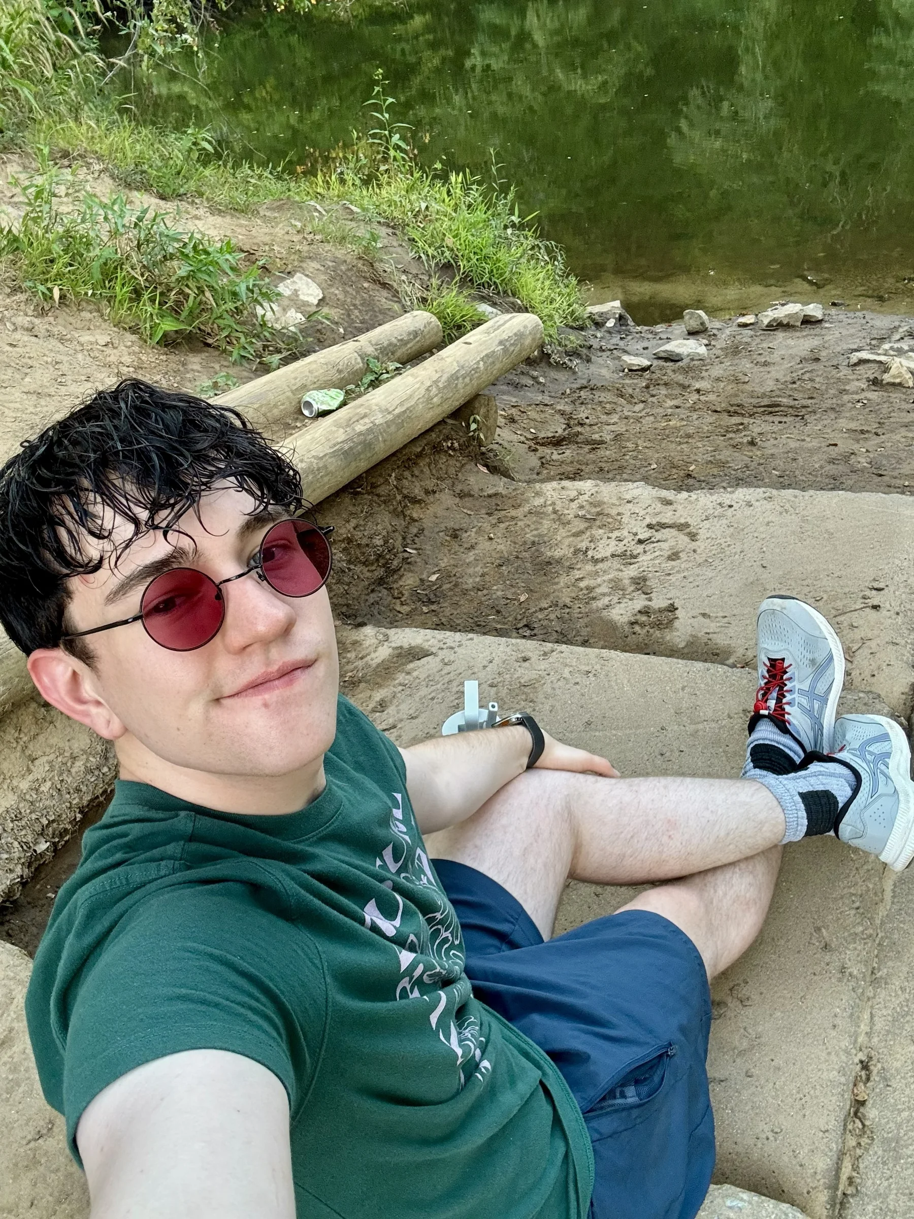 Drew seated beside a creek in a quiet wooded setting.