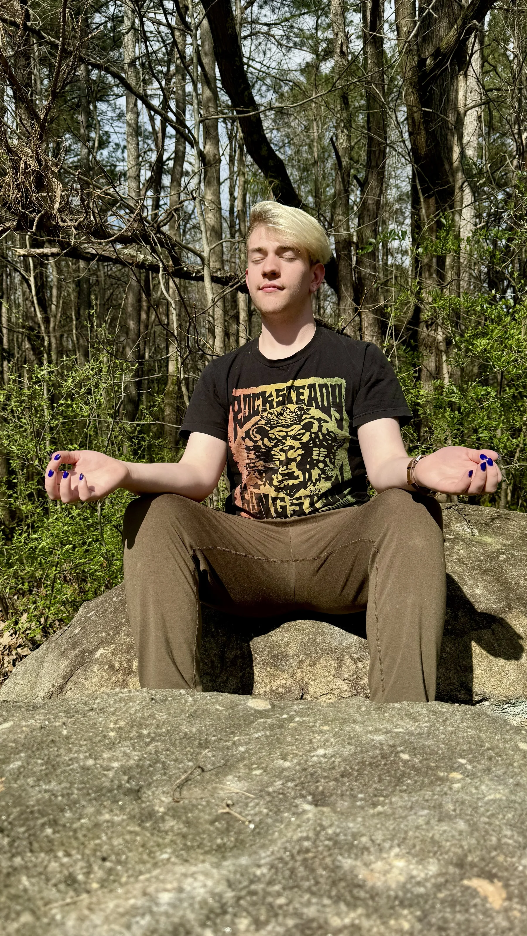 Drew meditating outside among trees and stone.