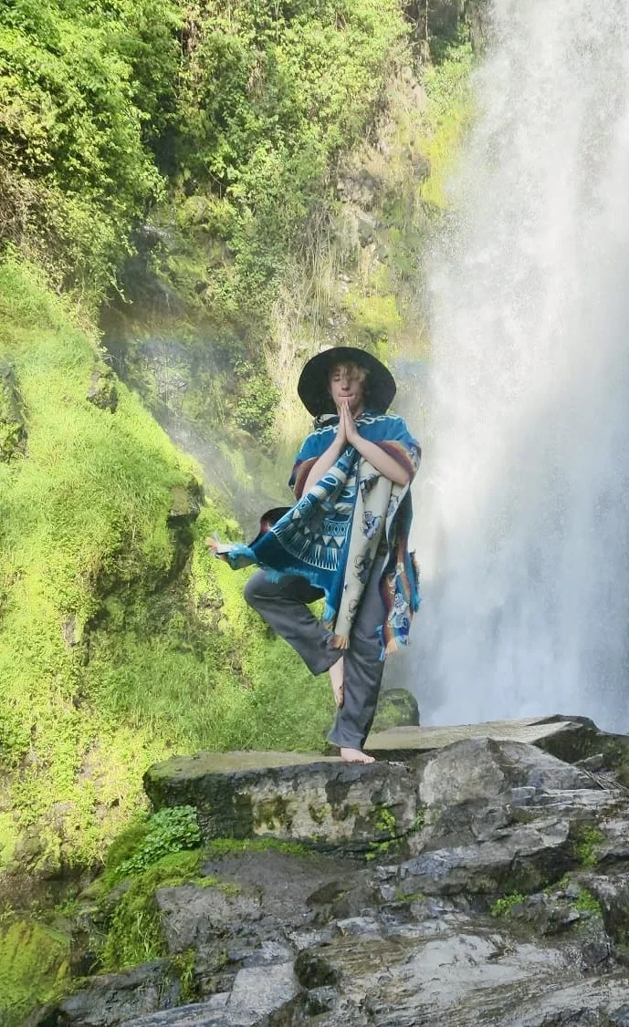 Drew standing near a misting waterfall in a bright, cinematic landscape.