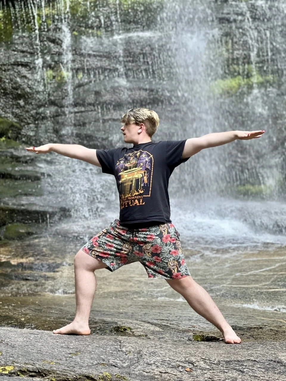 Drew practicing a grounded warrior pose beside a waterfall.