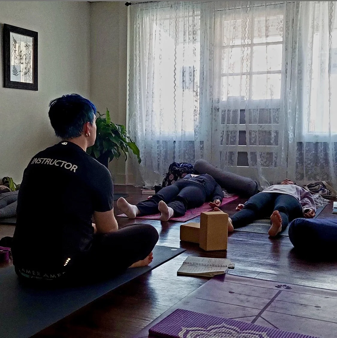 A restorative yoga session with students resting on mats as Drew supports the room.