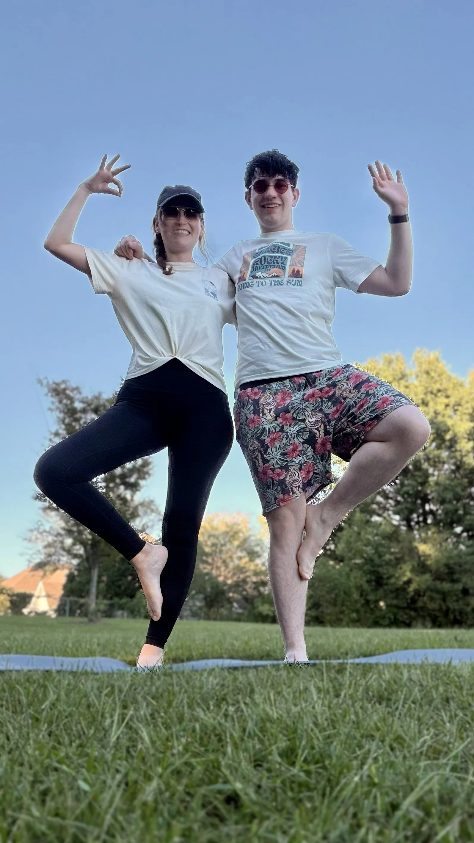 Two people balancing together in tree pose outdoors.