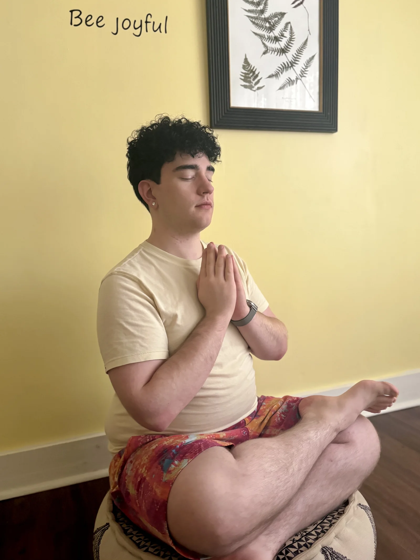 Drew seated in meditation with palms together at Bee Humble Studio.